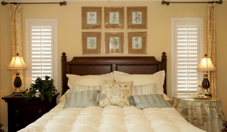 Tall plantation shutters framing bed in a bedroom in Jacksonville 